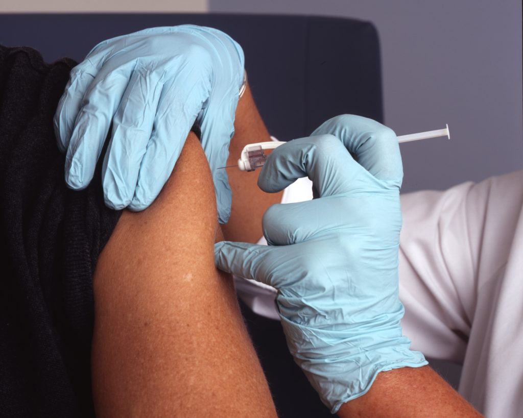 A person in blue gloves administers a vaccine to a person's arm. 