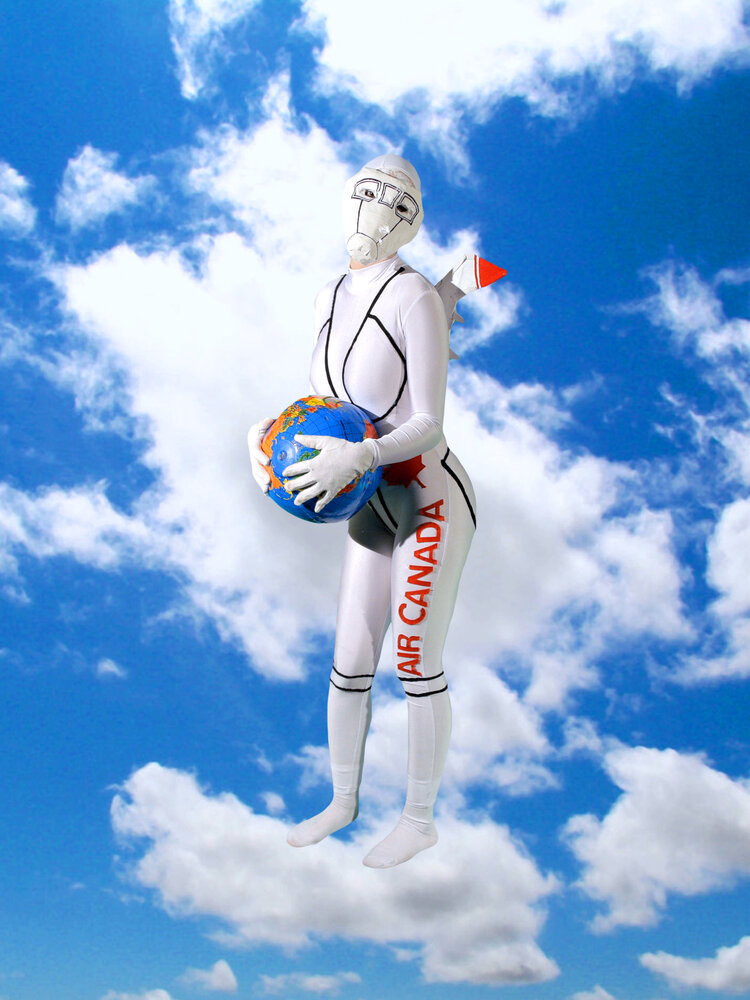 A person in a white suit that covers their face stands in front of an image of a blue sky with clouds, and is holding a blue aviation helmet.  