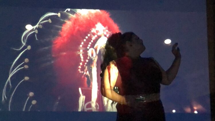 A person stands in front of a projection of an Indigenous headdress.