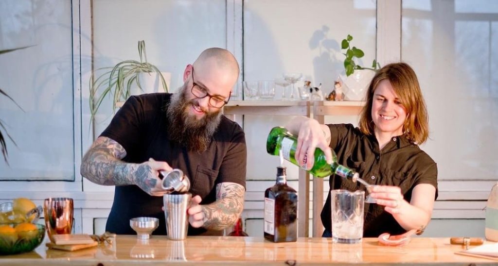 Glenn Barrington and Anne Herteis make drinks behind a bar, side by side.