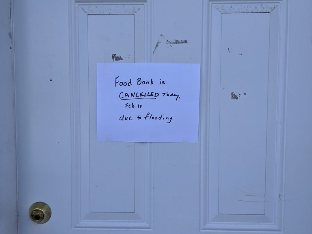 A paper sign taped to a door reads "Food bank is closed due to flooding."