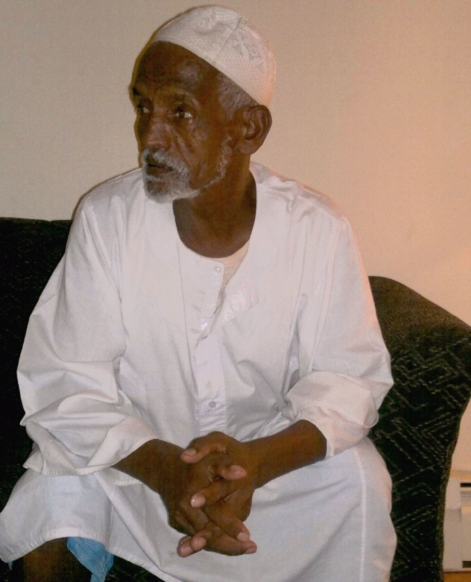 Abdulgadir Nur sits with his hands folded. He has brown skin and a short white beard.