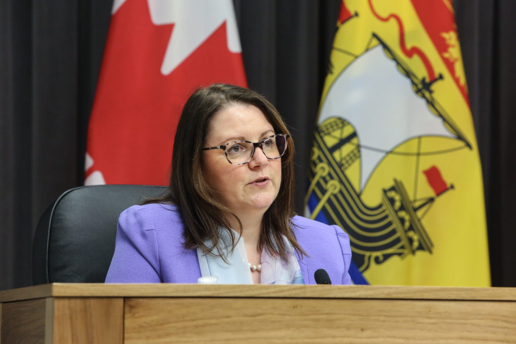 Dr. Jennifer Russell sits behind a podium and speaks. 