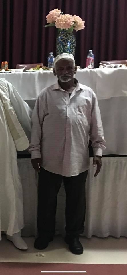 Abdulgadir Nur stands and smiles. He has brown skin and a short white beard.