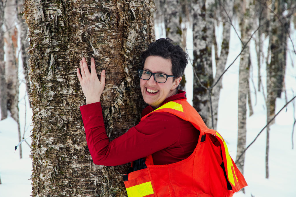 A woman hugs a tree while wearing an orange reflective vest.