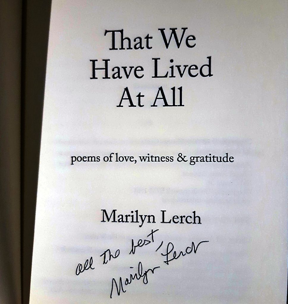 The inside jacket of a book reads "That We Have Lived At All, Marilyn Lerch." A handwritten signature reads "All the best, Marilyn Lerch."