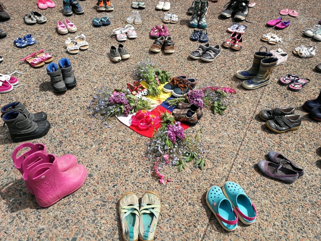 Childrens' shoes surround flowers placed on pavement.