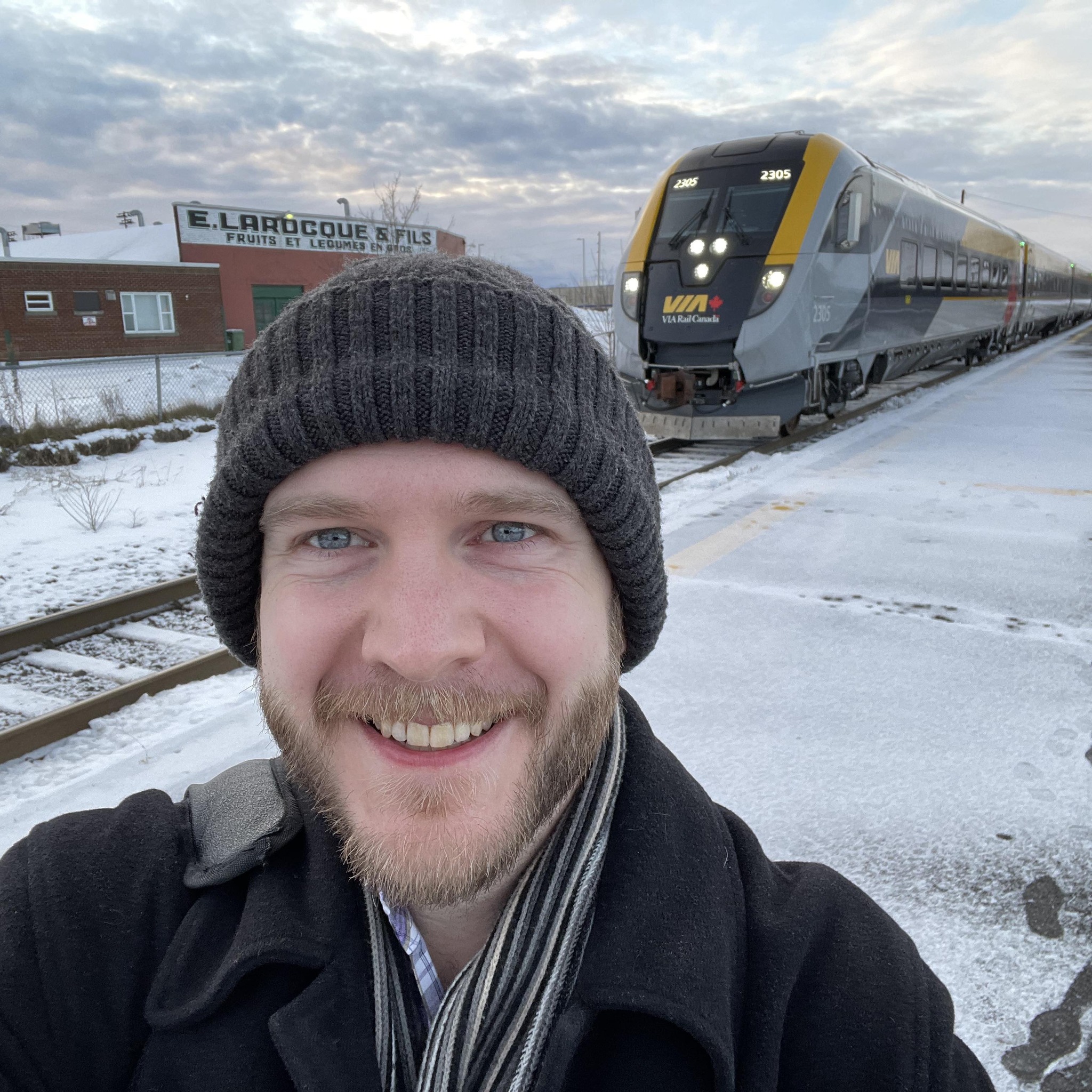 A man in a toque, standing outside in the winter with a VIA Rail train in the background.