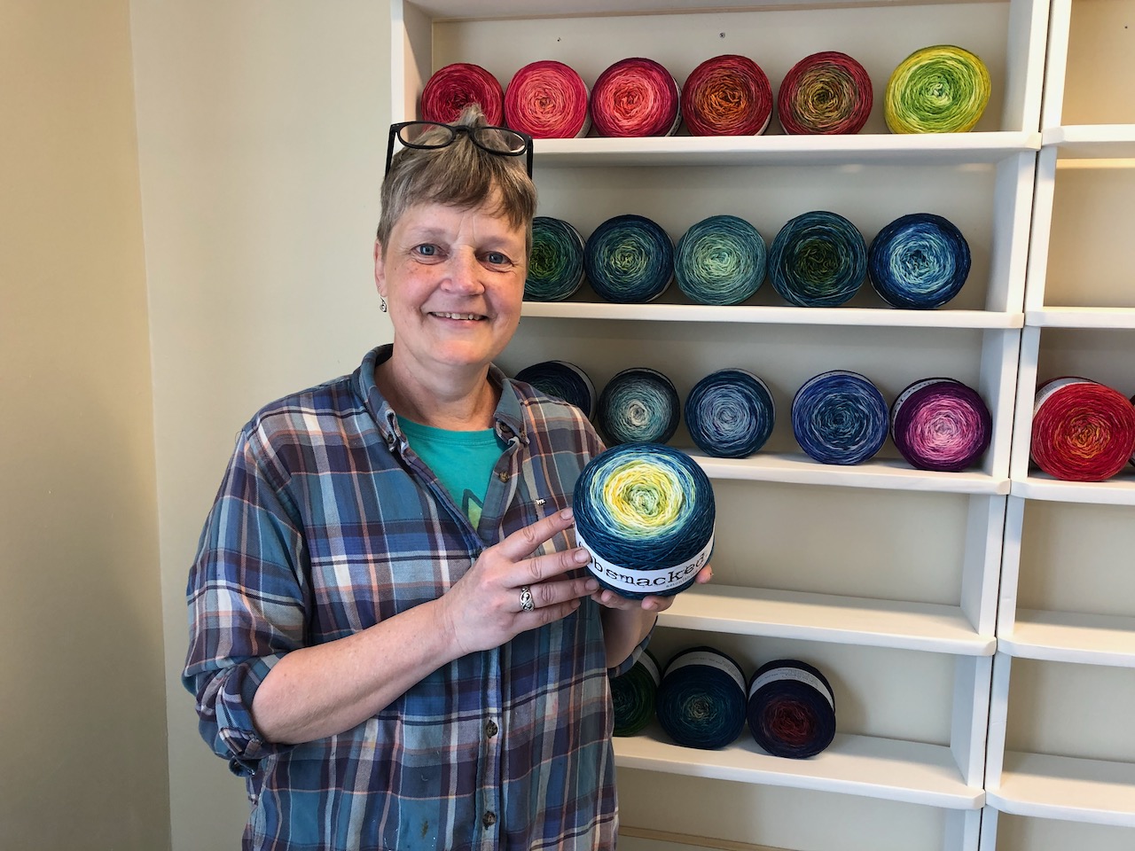 A woman stands holding a spool of yarn, in front of shelves filled with many different colours of similar spools