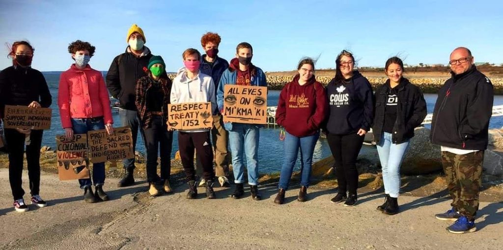 Divest Mount A and Indigenous Student Support Group members stand in a line holding protest signs for Mi'kma'ki.