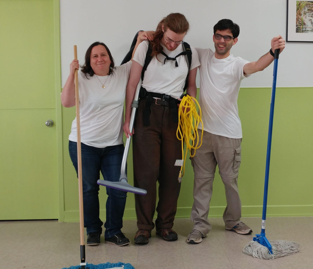 Three members of Powerhouse Co-op wear matching T-shirts and are holding cleaning equipment.