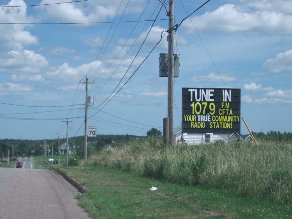 A road sign reads "Tune in 107.9 FM CFTA, You're true community radio station." 