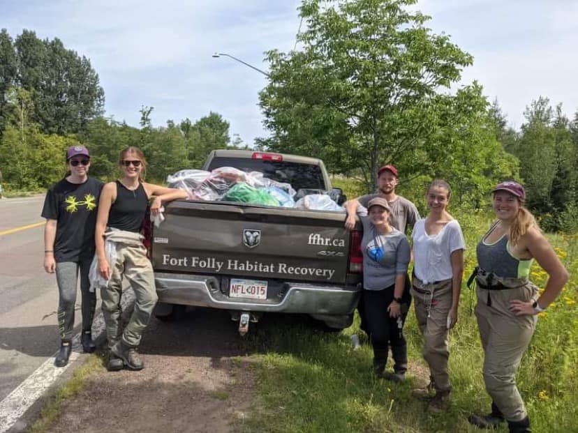 People stands around a pick-up truck full of bags of garbage, outdoors.