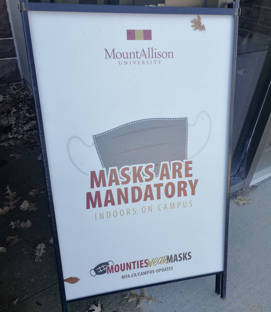 Sign saying "masks are mandatory" with the Mount Allison logo and a picture of a COVID face mask.