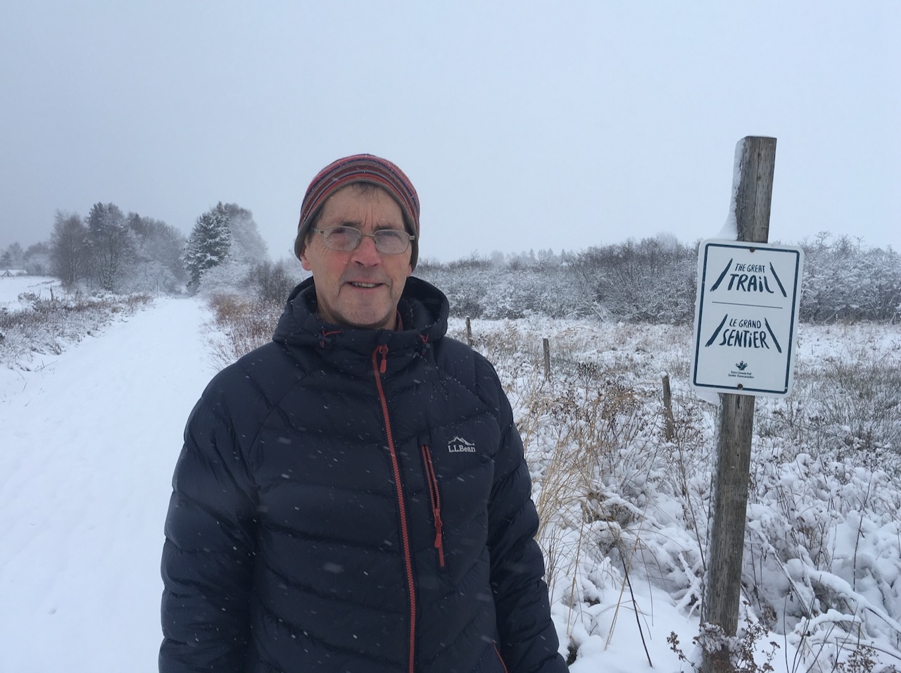 Man stands on a snowy trail with sign post reading The Great Trail.