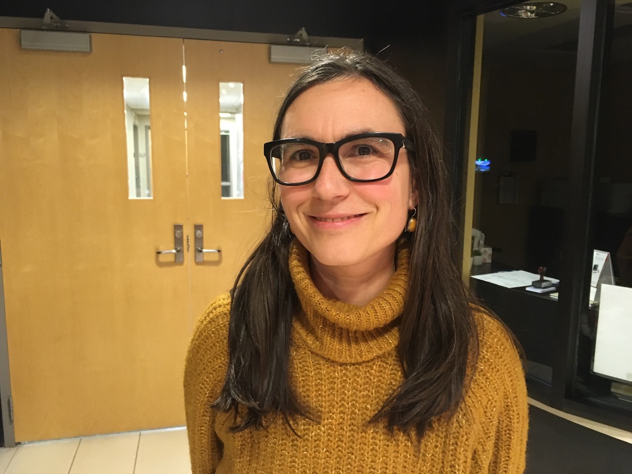 Woman in glasses, with long hair, smiling at camera